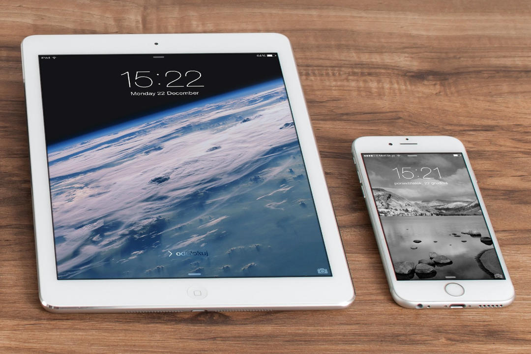 Ein iPad und ein iPhone liegen auf einer Holzplatte. Auf den Geräten sind unterschiedliche Startbildschirme erkennbar.